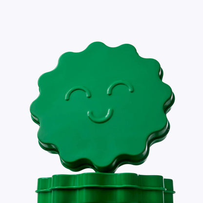 A bright green, flower-shaped container lid with a smiling face, shown resting on top of a matching green cylindrical base against a light gray gradient background.